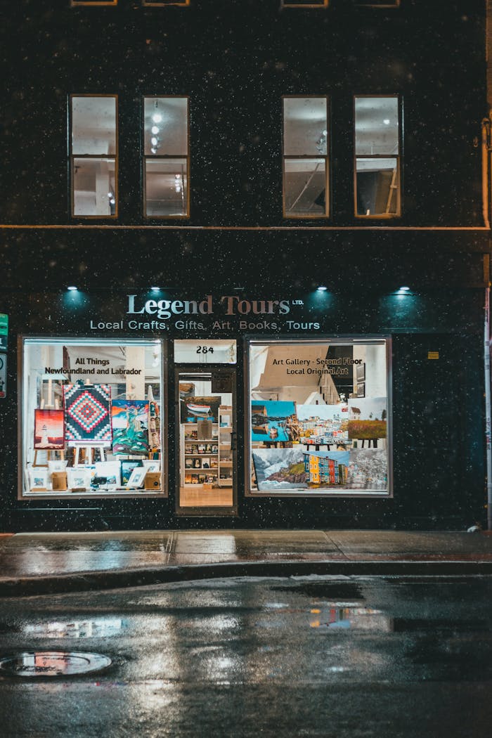 Exterior of touristic shop and travel agency with pictures and souvenirs in windows with illuminated sign above at night